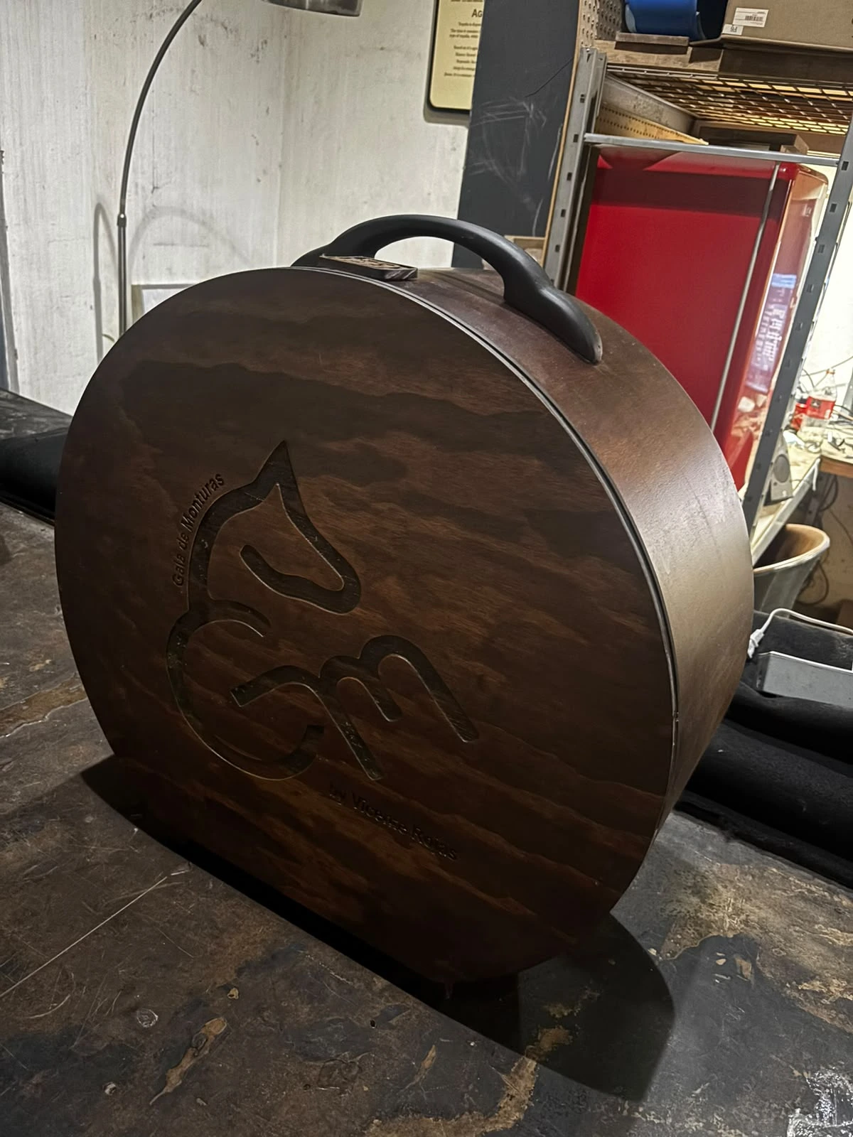 Estuche circular de madera oscura con logotipo de caballo grabado y asa