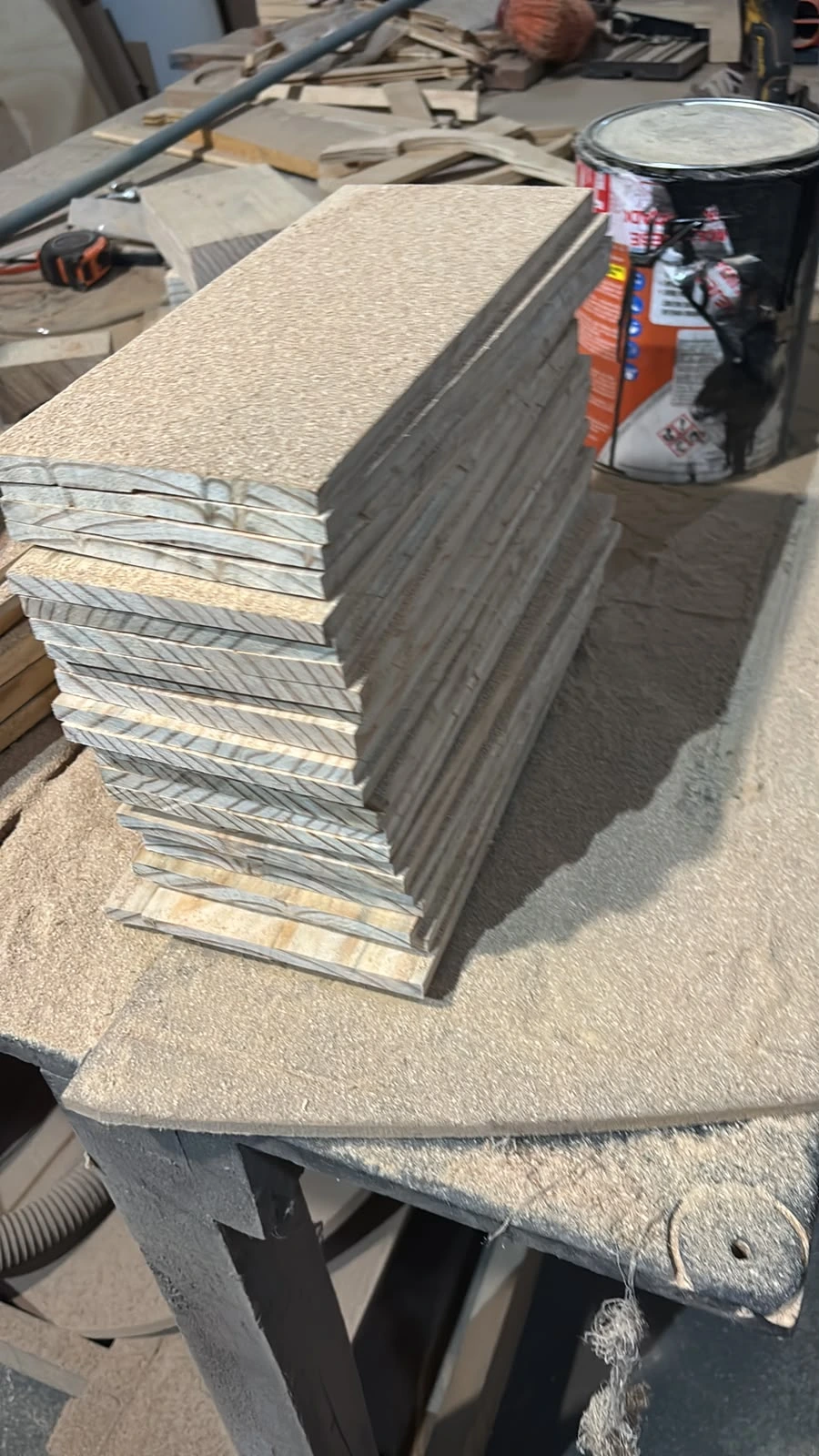 Listones de madera con cortes de curvado kerf apilados junto a una lata de barniz