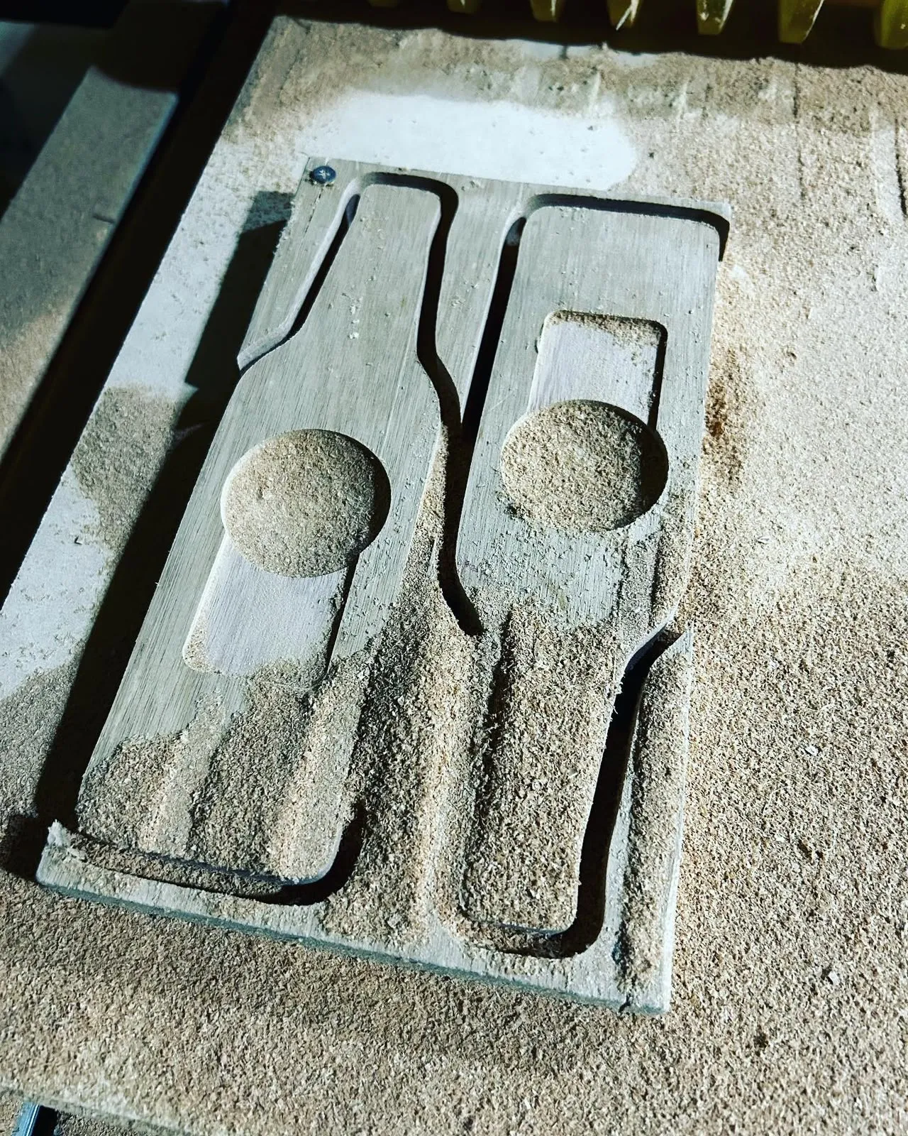 Router CNC tallando el alojamiento de una botella y una copa sobre un tablero cubierto de aserrín